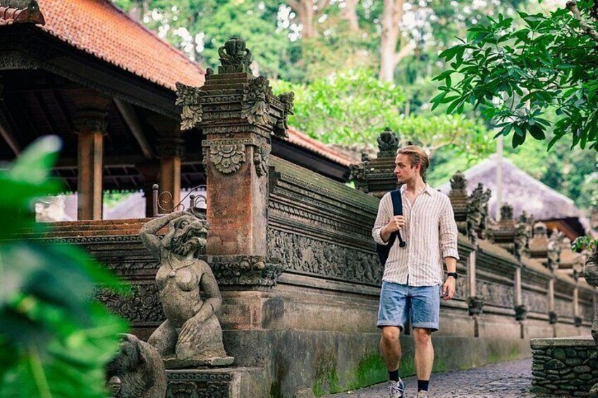 A man walking near a stone structure with intricate carvings, surrounded by lush greenery. 4