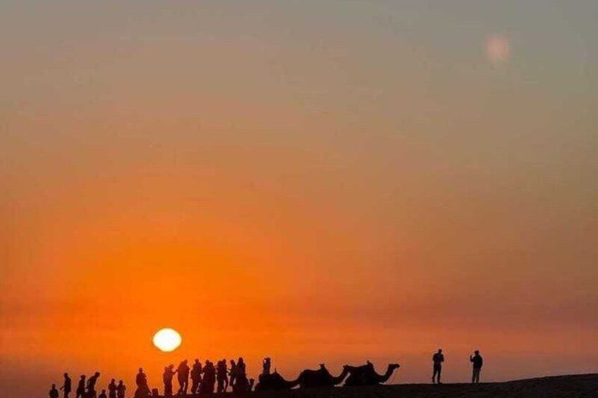 A sunset over a desert landscape with silhouettes of people and camels. 4