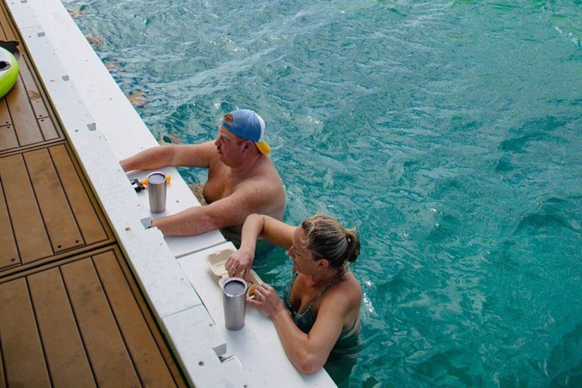 Two people sitting at a poolside table with drinks. 2