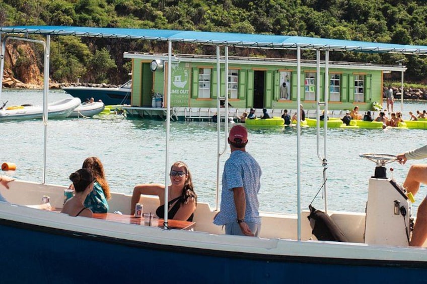 Un bote con gente a bordo, un muelle con un edificio verde y un área de piscina donde nadan personas. 2