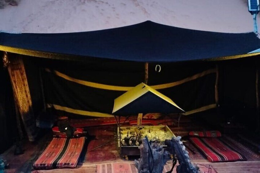 A tent with a black and yellow canopy, a central table, and red and black striped rugs. 2