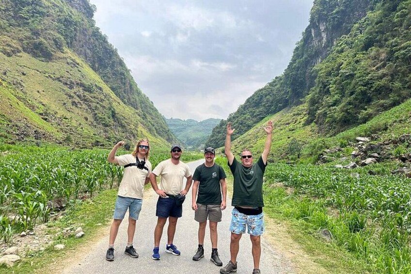 Four people standing on a path surrounded by lush greenery and hills. 3