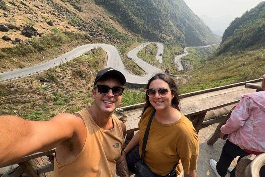 A person taking a selfie with a scenic mountainous landscape and winding roads in the background. 5