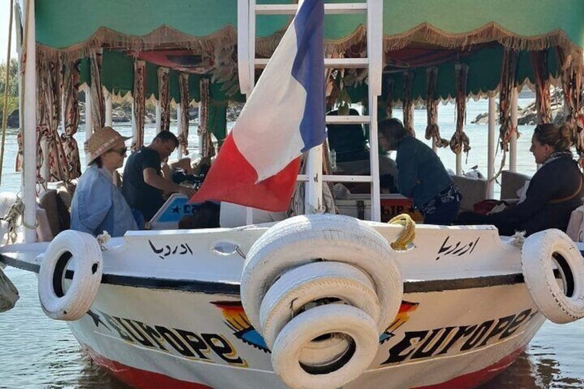 A boat with a flag, people on board, and a cabin structure. 1