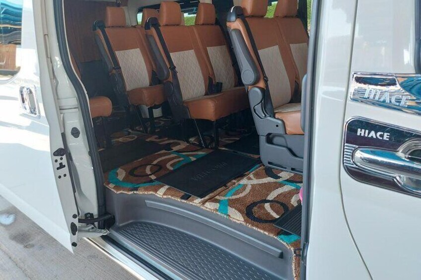 A van interior with brown and beige seats, a patterned floor mat, and a 'HIACE' logo on the door. 2
