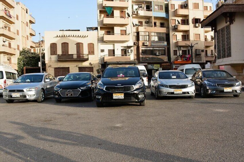 A row of parked cars in an urban street with multi-story buildings in the background. 4