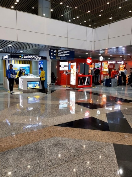 A modern airport terminal with a polished floor, a Celcom Digi kiosk, and a Tune store. 4