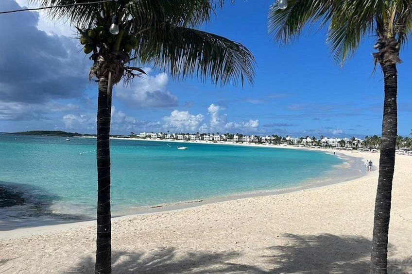 Una playa con aguas turquesas cristalinas, palmeras y una costa distante con edificios. 2