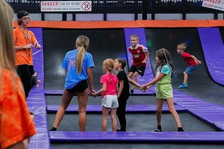 Children playing on a trampoline with safety signs and an adult supervising. 1