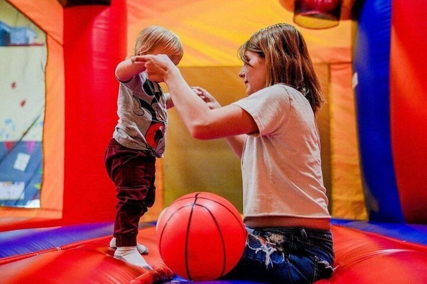 A child and an adult on a colorful inflatable bounce house with a basketball. 2