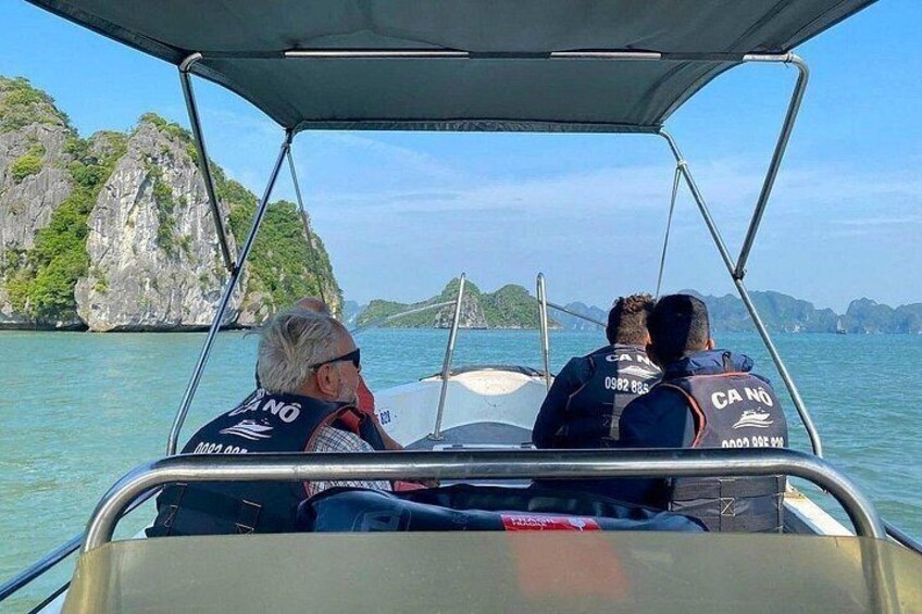 Tres personas en un bote, con la inscripción 'CA NO' en sus chaquetas, rodeadas de agua y acantilados rocosos. 3