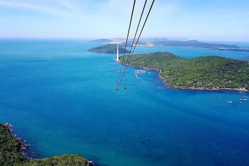 A cable car system over a coastal area with clear blue waters and green hills. 1