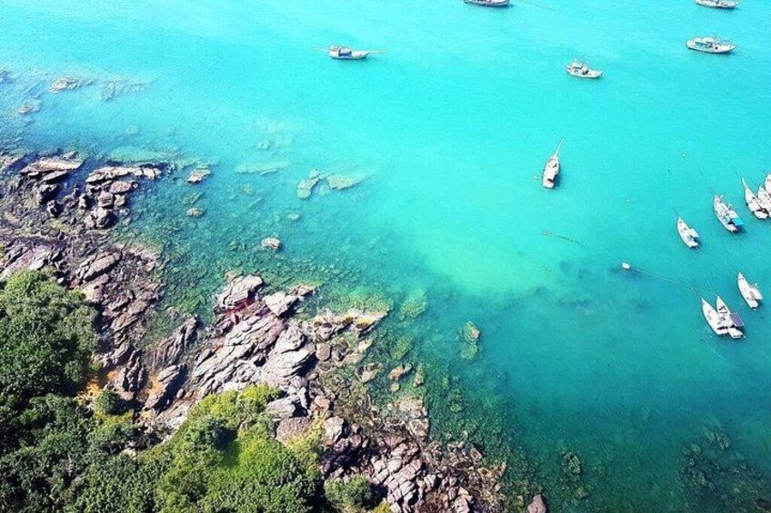 A coastal area with clear turquoise waters, rocky outcrops, and numerous boats anchored near the shore. 4