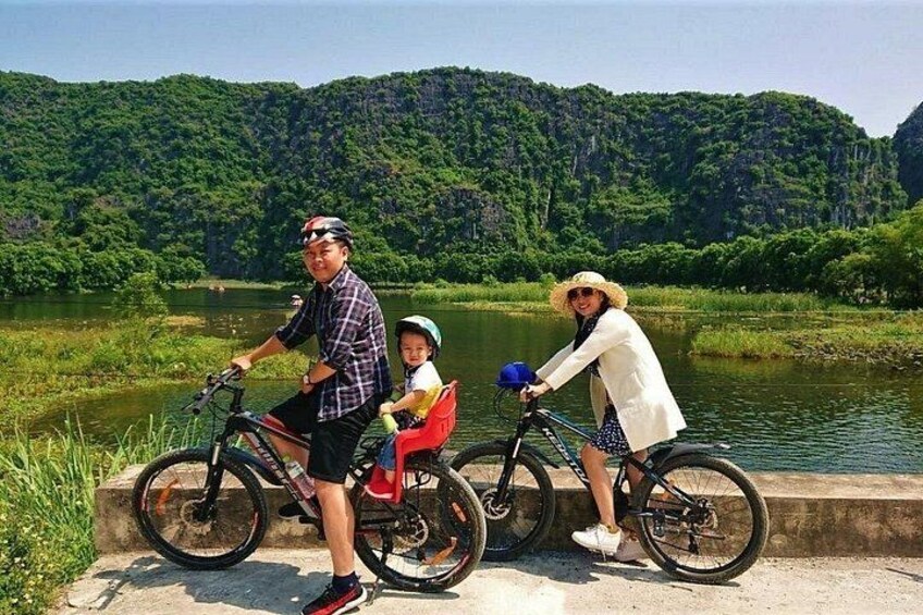 Una famiglia in bicicletta lungo un fiume, con il verde sullo sfondo. 1