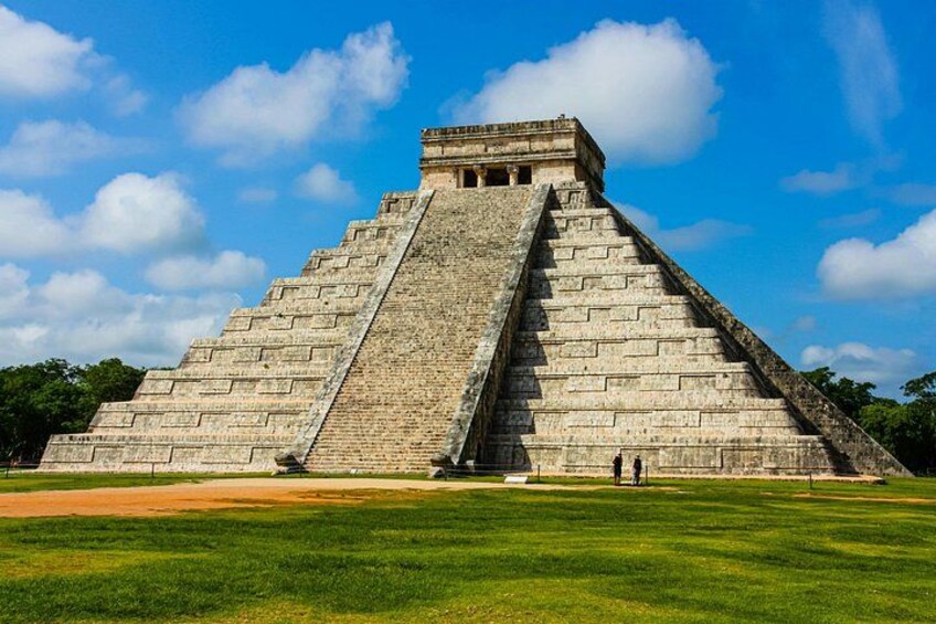 A large pyramid structure with a wide base and a steep incline, surrounded by a grassy field and trees under a clear sky. 1