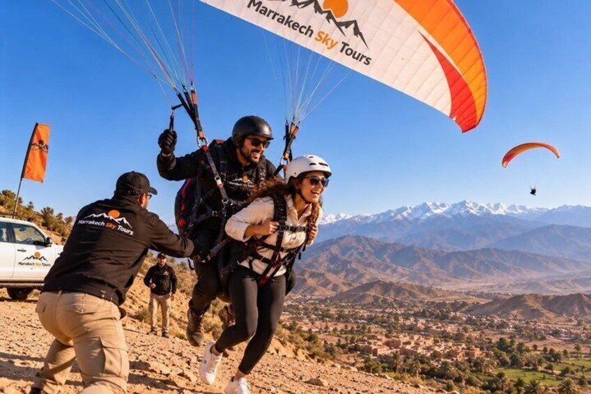 A person being assisted with a parachute, a mountainous landscape, and a clear sky. 2