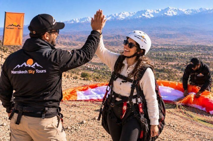 A person giving a high-five to another person wearing a helmet, with a mountainous landscape in the background. 5