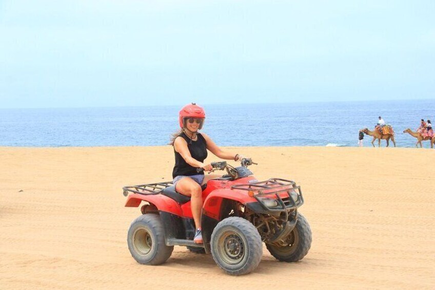Een persoon rijdt op een rode quad over een zandstrand, met de oceaan op de achtergrond. 4