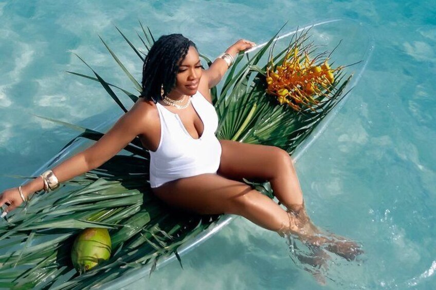 A person in a white swimsuit sitting on a boat in a clear blue pool with green plants and a yellow flower. 3