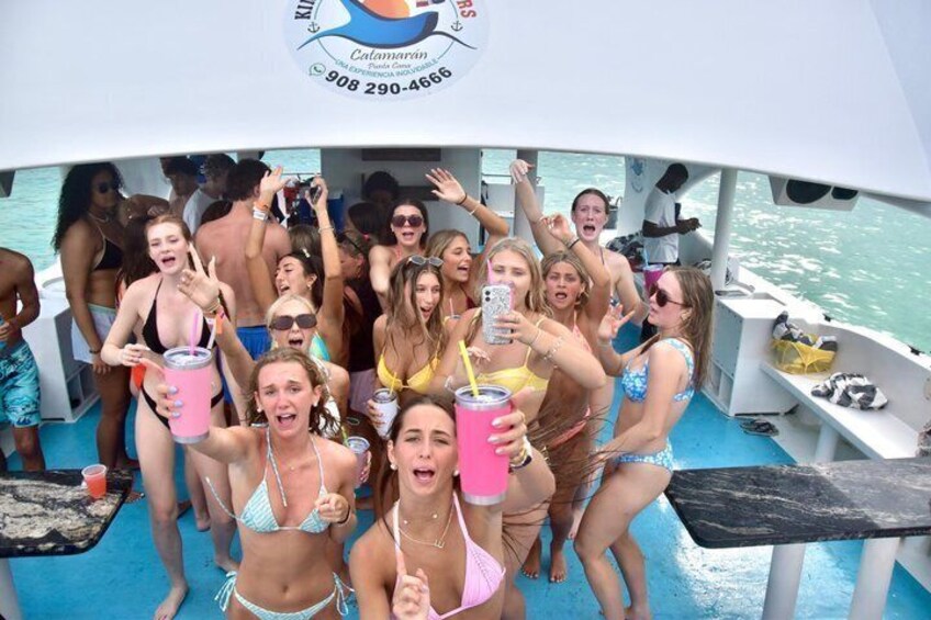 A group of people on a boat with drinks, a logo, and a phone. 5