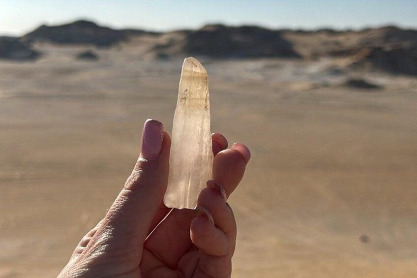 A hand holding a clear quartz crystal against a desert landscape. 4