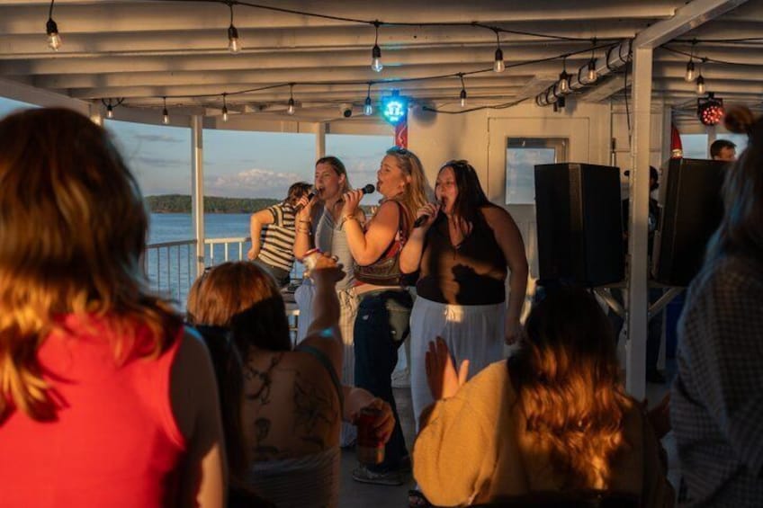 A group of people singing on a boat with a lake in the background. 4