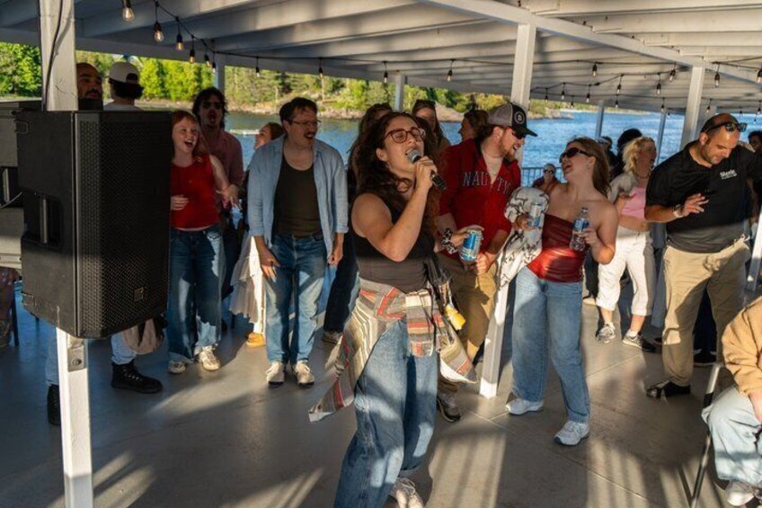 A group of people on a boat with a speaker and a person singing. 1