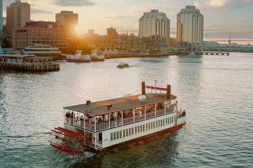 A riverboat with passengers, docked near a city skyline with grain silos in the background. 5