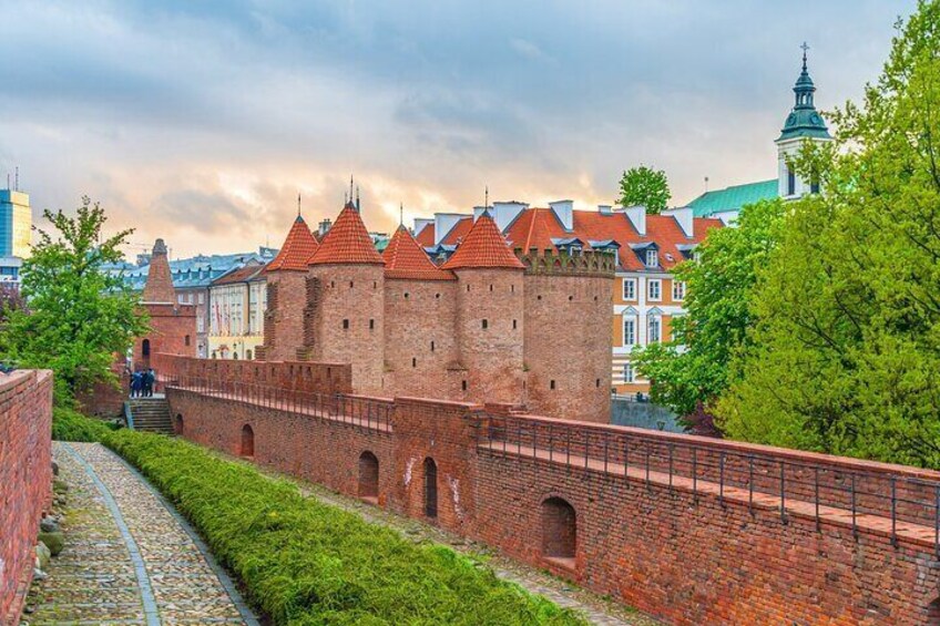 A historic brick wall with towers, a paved walkway, and modern buildings in the background. 3