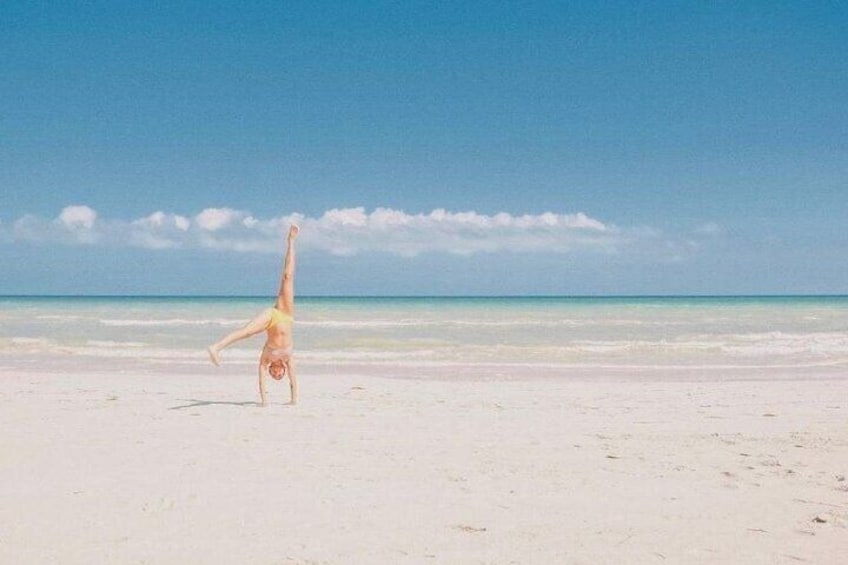 Una persona haciendo una postura de equilibrio de manos sobre la playa, con un cielo despejado y un mar tranquilo al fondo. 5