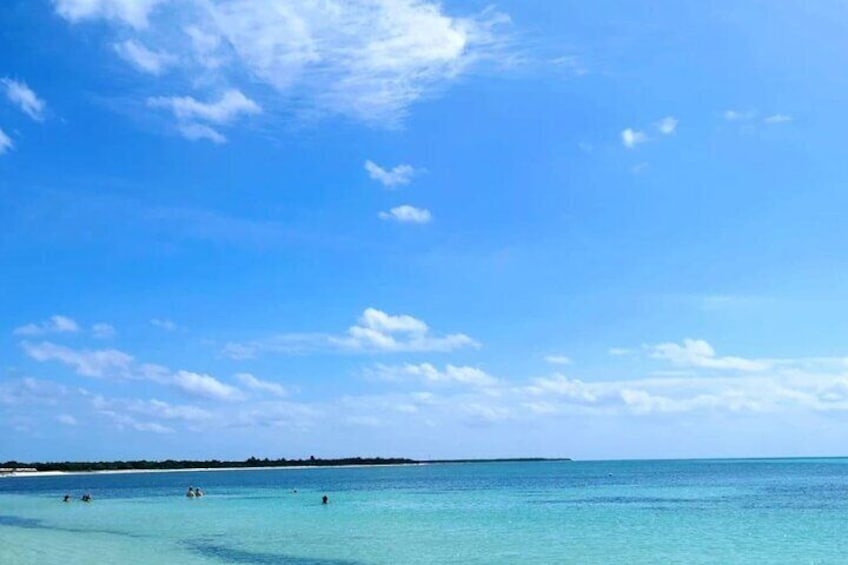 Cielo azul despejado, mar tranquilo y una costa lejana con gente nadando. 2