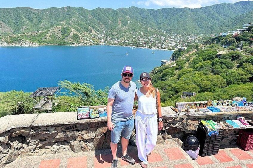 A couple standing on a stone wall overlooking a lake with mountains in the background. 4