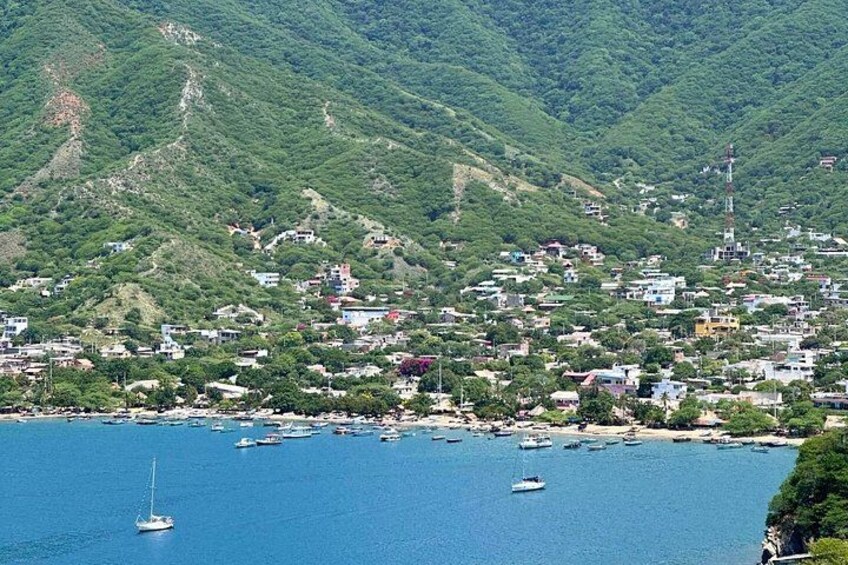 A coastal town with buildings, boats, and lush green hills. 1