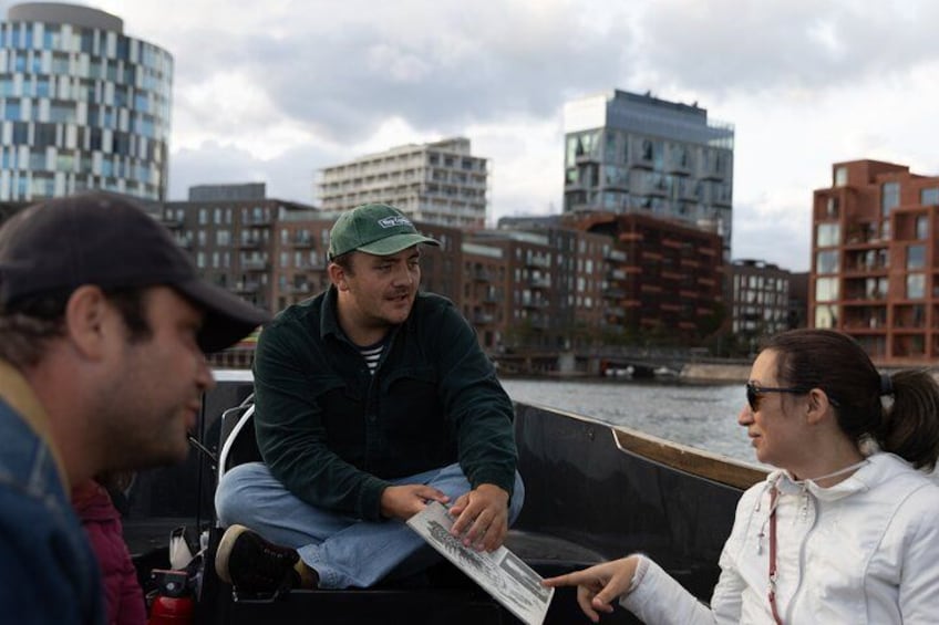 Eine Gruppe von Menschen auf einem Boot, im Hintergrund eine Stadtansicht. 2