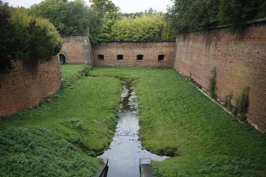 A narrow water channel flanked by brick walls, with grass on either side and a small bridge in the center. 4
