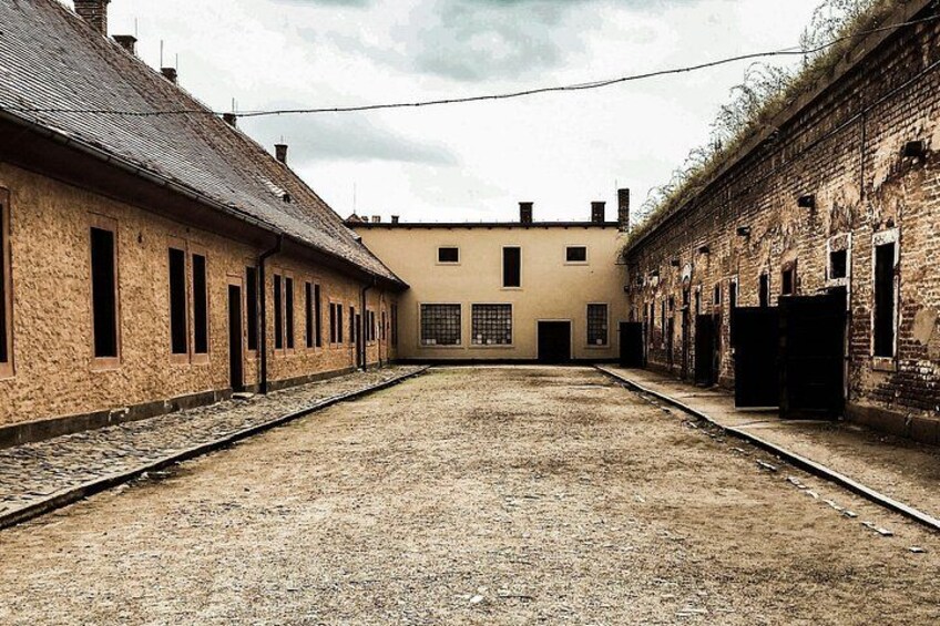 A deserted train station with two tracks, old brick buildings, and a clear sky. 1