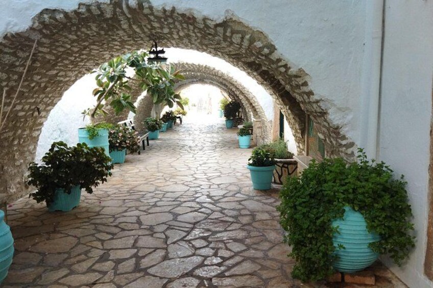 An arched stone corridor with potted plants lining the path. 2