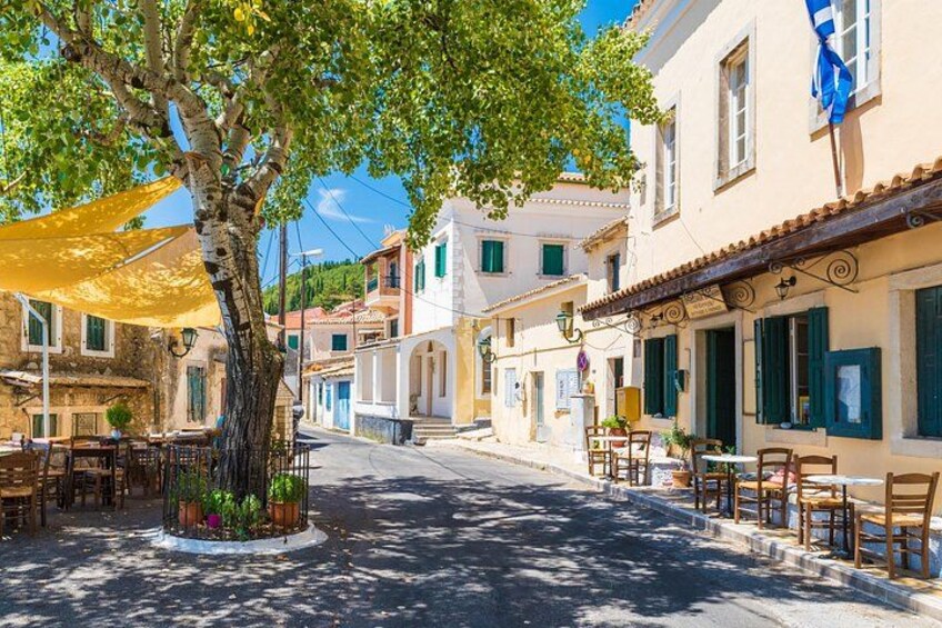 A tree-lined street with outdoor seating, buildings with shutters, and a clear blue sky. 5