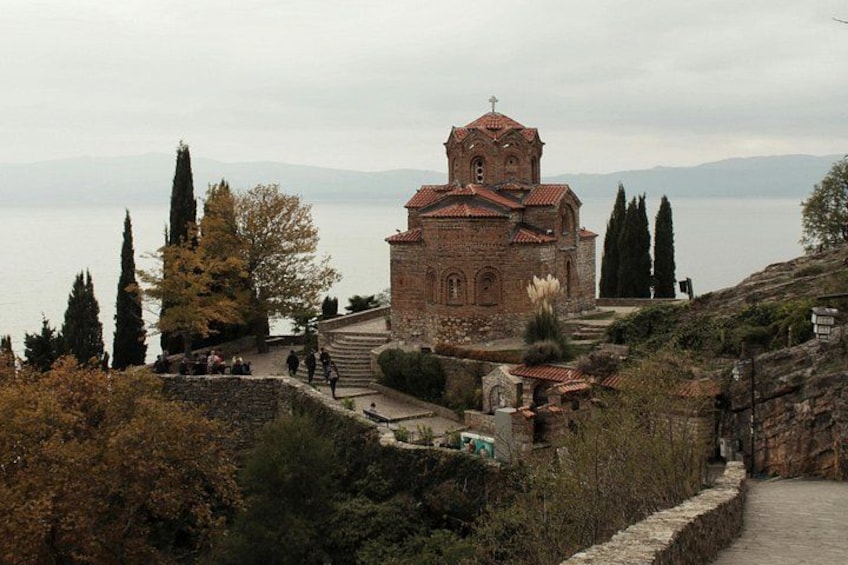 A historic church with a bell tower, surrounded by trees and a body of water in the background. 1