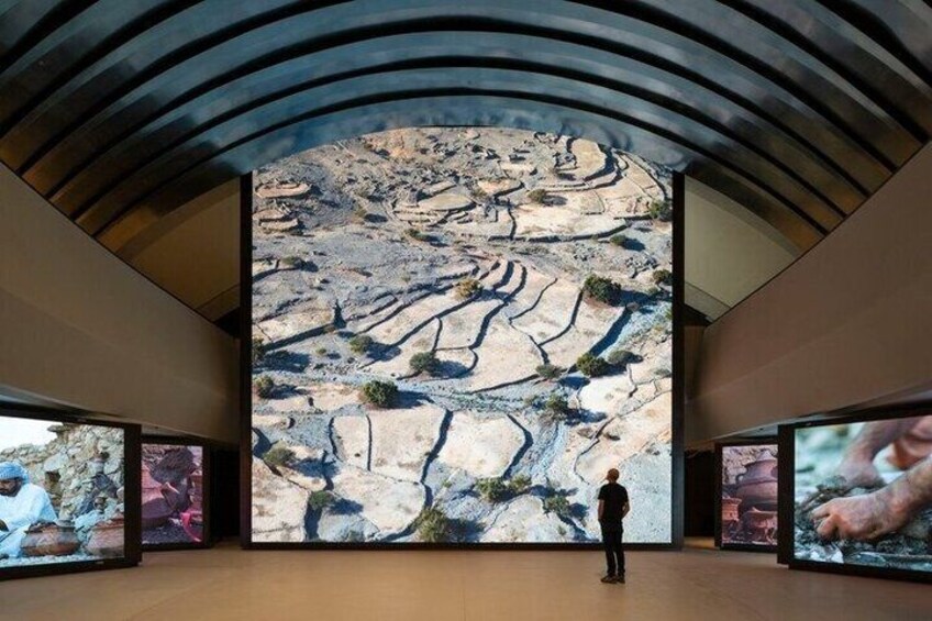 A person standing in a gallery with large wall-mounted screens displaying geological formations. 4
