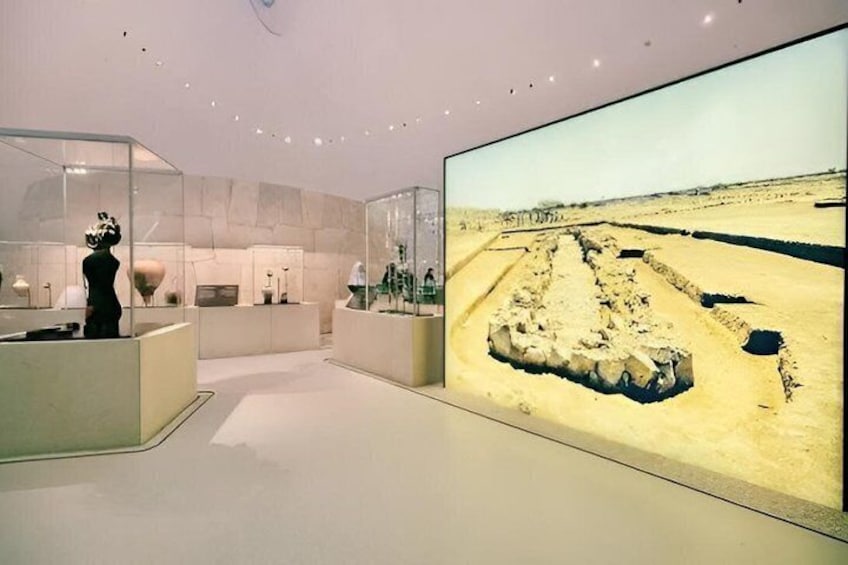 An indoor museum with a large screen displaying an excavation site. 3