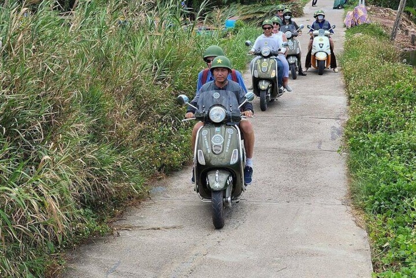 A group of people on scooters on a narrow path surrounded by tall grass. 5