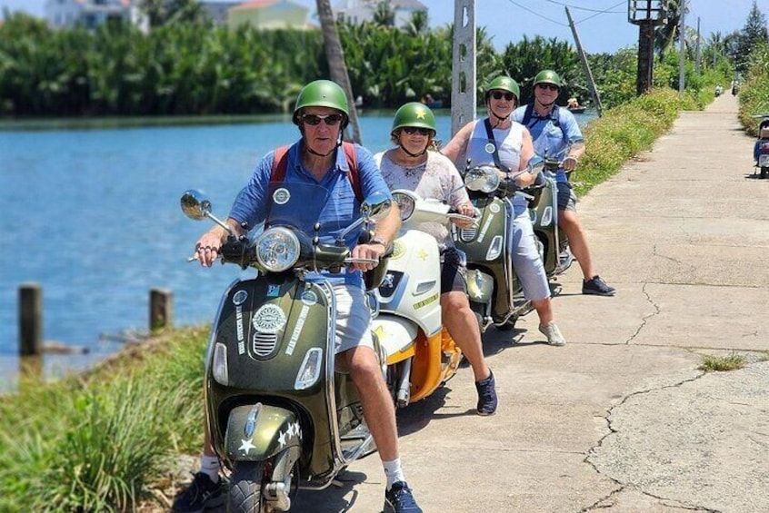 A group of people riding scooters along a paved path by a body of water. 3