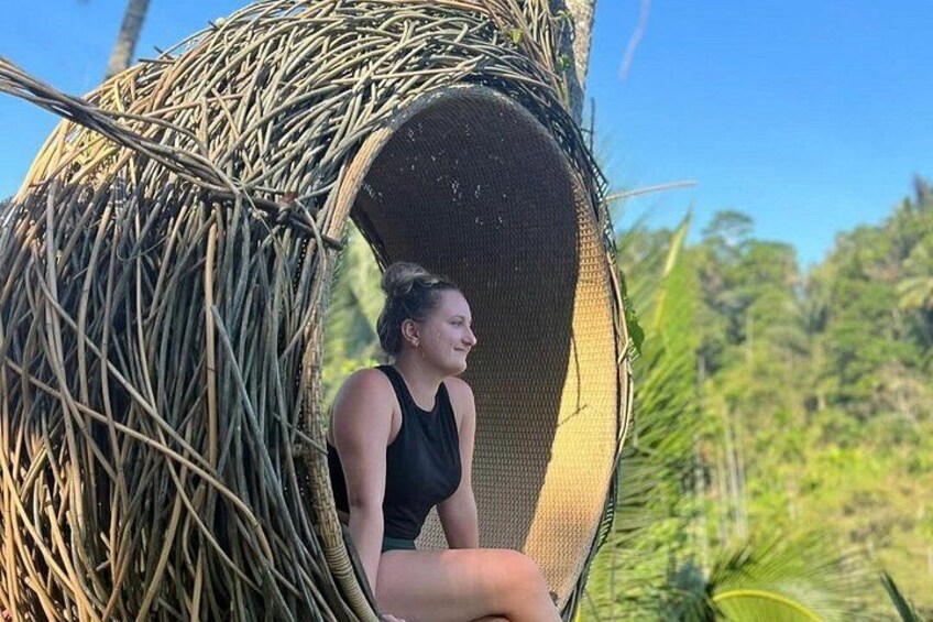 A person sitting in a woven basket-like structure outdoors. 2