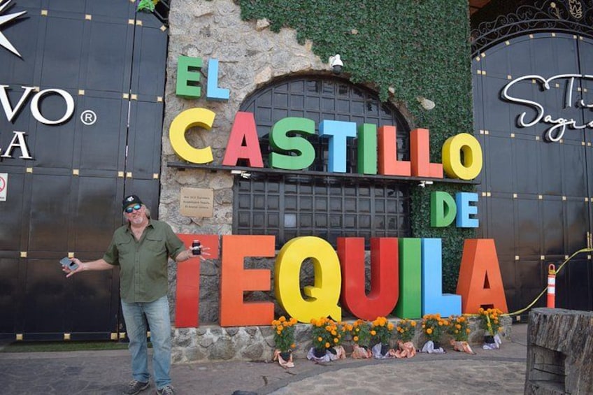 En mand står foran et farverigt skilt med teksten 'EL CASTILLO DE TEQUILA'. 1