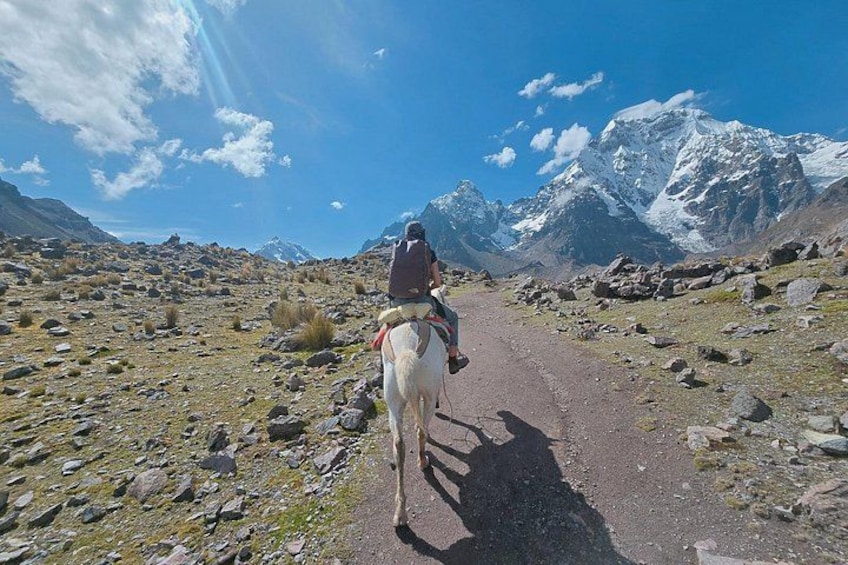 Une personne à cheval, sur un sentier rocailleux, avec des montagnes en arrière-plan. 1