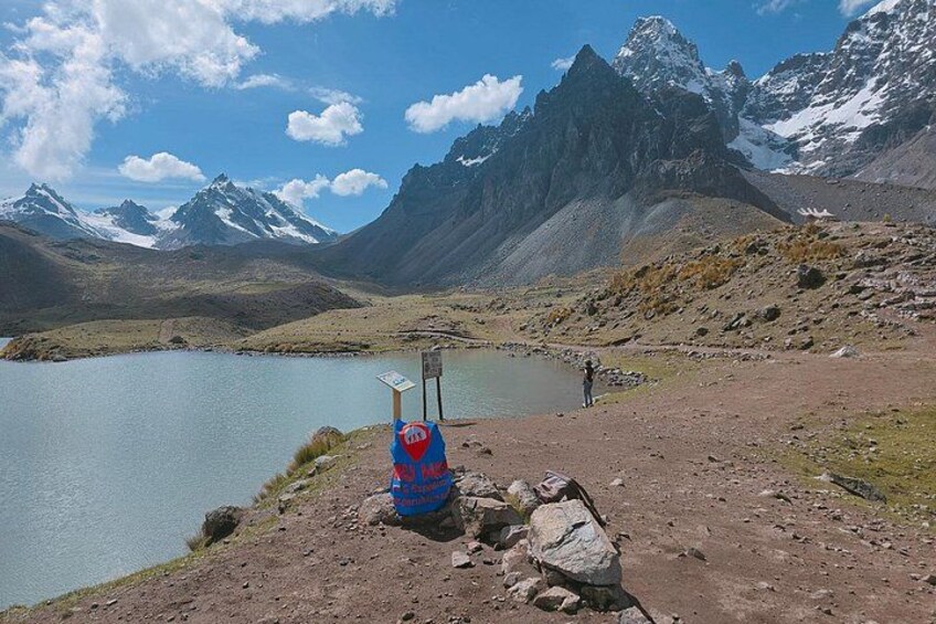 Un paysage montagneux avec un lac, une rive rocheuse et une personne debout près d’un panneau bleu. 2
