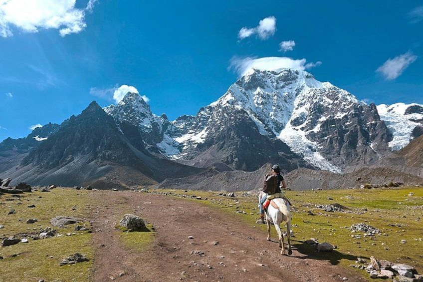 Une personne à cheval sur un sentier de terre, avec des montagnes enneigées en arrière-plan. 1