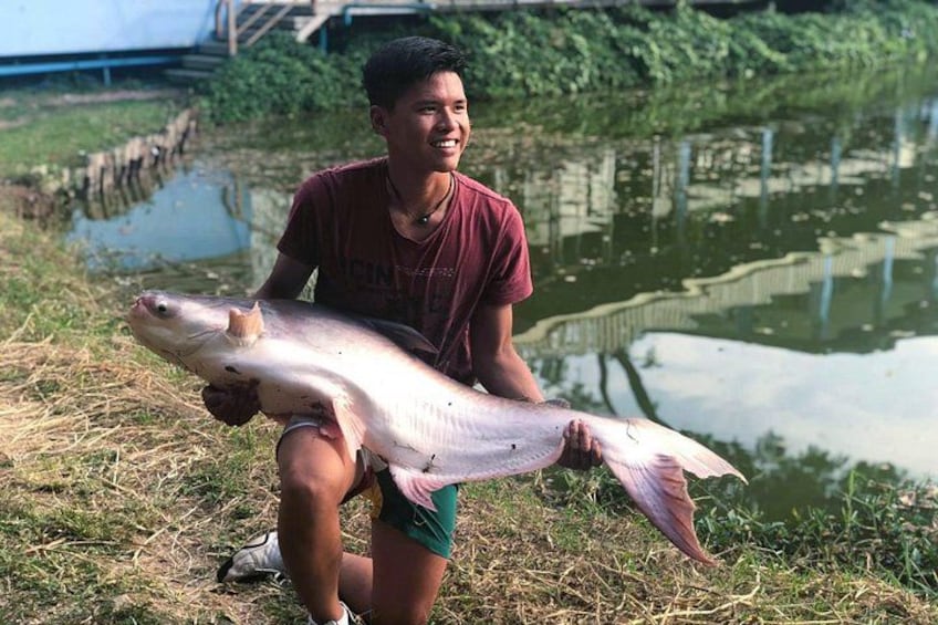 A person holding a large fish by a body of water. 5