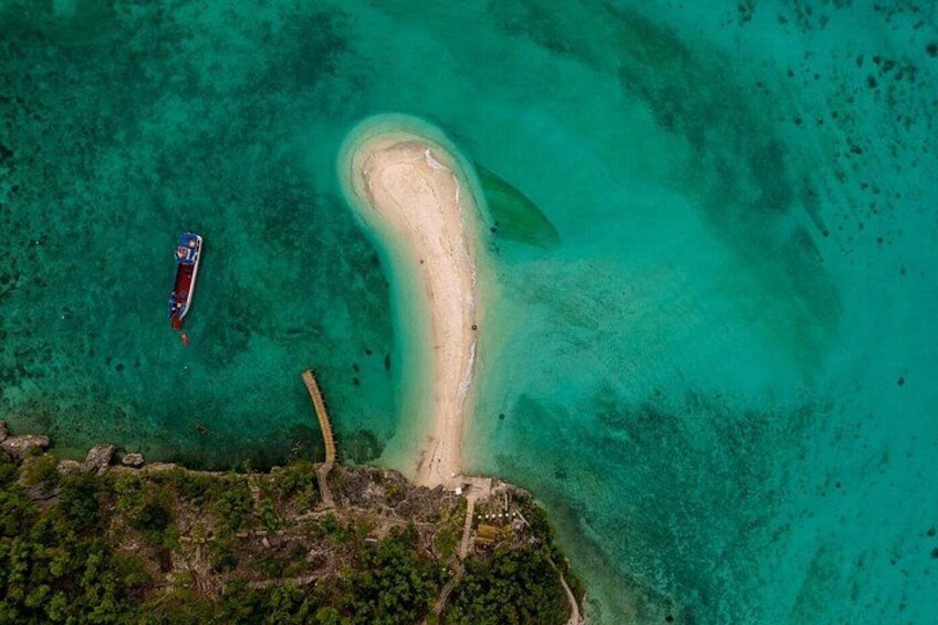 An aerial view of a turquoise lagoon with a sandy beach, a boat, and a small island with vegetation. 2